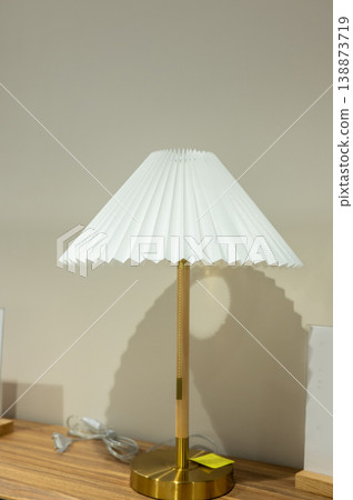 Elegant brass table lamp with white pleated shade on wooden surface Elegant brass table lamp with white pleated shade on wooden surface 138873719