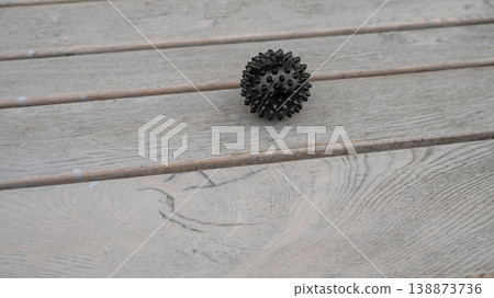 Black spiky massage ball on wooden deck surface 138873736
