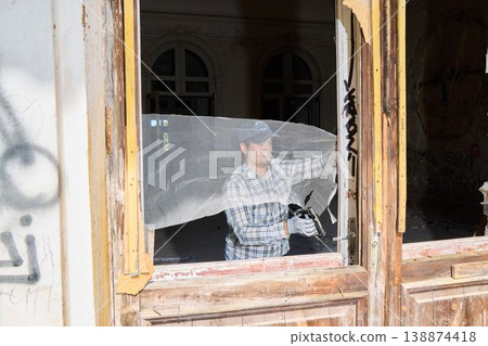 Maintenance worker securing mesh to old window structure in daylight Maintenance worker securing mesh to old window structure in daylight 138874418
