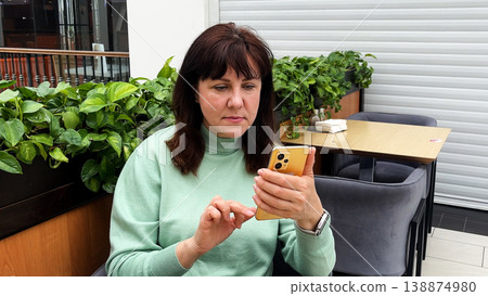 Middle-aged woman sitting in a coffee shop using her smartphone. Middle-aged woman sitting in a coffee shop using her smartphone. 138874980
