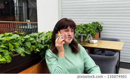 Middle-aged woman sitting in a coffee shop talking on her mobile phone Middle-aged woman sitting in a coffee shop talking on her mobile phone 138874981