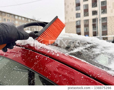 a girl cleans her personal car from snow with a black-and-orange car brush in the courtyard of an apartment building a girl cleans her personal car from snow with a black-and-orange car brush in the courtyard of an apartment building 138875266