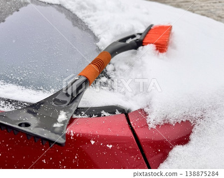 car brush with a scraper in black and orange on a background of snow-white snow on a car in winter 138875284