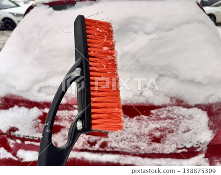 car brush with a scraper in black and orange on a background of snow-white snow on a car in winter 138875309