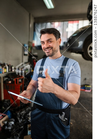 Car mechanic holding tablet and showing thumbs up in auto repair shop 138876247