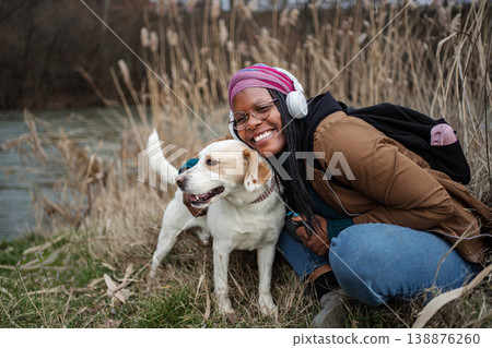 Smiling woman embracing her dog outdoors wearing headphones Smiling woman embracing her dog outdoors wearing headphones 138876260