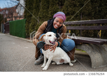 Happy young woman petting dog on park bench Happy young woman petting dog on park bench 138876264