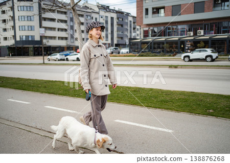 Young woman walking pet dog on urban street Young woman walking pet dog on urban street 138876268