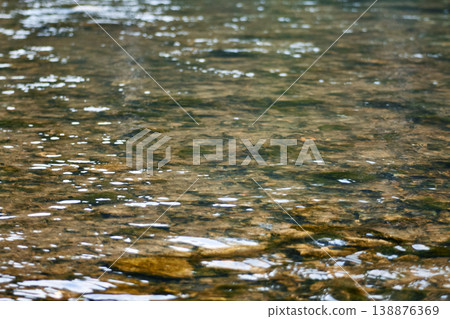 Clear water flowing over smooth stones in a river bed. Natural texture of creek bottom with ripples and reflections. Environmental concept of clean stream, wildlife and wilderness. Clear water flowing over smooth stones in a river bed. Natural texture of creek bottom with ripples and reflections. Environmental concept of clean stream, wildlife and wilderness. 138876369