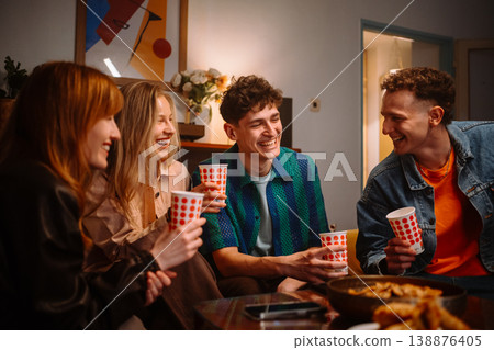 Cheerful group of young diverse friends laughing and toasting with cups at a cozy home party Cheerful group of young diverse friends laughing and toasting with cups at a cozy home party 138876405