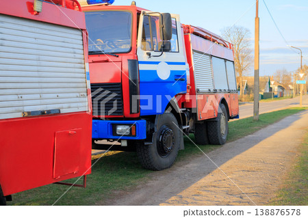 Red fire trucks stand on the side of a country road. 138876578