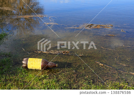 Plastic bottle discarded in shallow river water near the grassy bank. Environmental pollution and water contamination concept. Plastic bottle discarded in shallow river water near the grassy bank. Environmental pollution and water contamination concept. 138876586