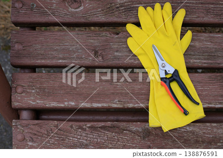 Yellow rubber gardening gloves and a sharp pruner lying on a dark wooden bench. Professional horticulture tools prepared for spring plant care Yellow rubber gardening gloves and a sharp pruner lying on a dark wooden bench. Professional horticulture tools prepared for spring plant care 138876591