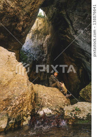 Hiker Resting inside Large Cave during Outdoor Adventure Hiker Resting inside Large Cave during Outdoor Adventure 138876641