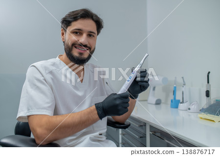 Dark-haired young dentist in his office looking confident and busy Dark-haired young dentist in his office looking confident and busy 138876717