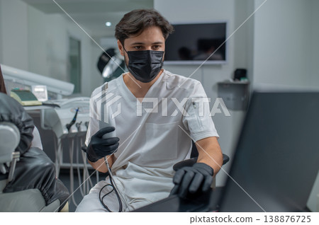 Male dentist in protective mask working in his office and looking confident 138876725