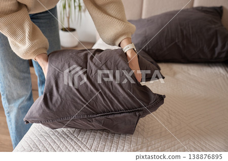 Person arranging dark pillow on bed in bedroom interior. Concept of bedding change 138876895