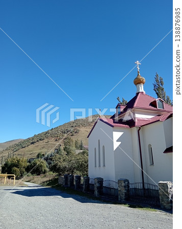 Stone Alan Monastery, North Ossetia, Russia, bright summer day. Ancient stone monastic complex built into a green mountain slope under a clear blue sky Stone Alan Monastery, North Ossetia, Russia, bright summer day. Ancient stone monastic complex built into a green mountain slope under a clear blue sky 138876985