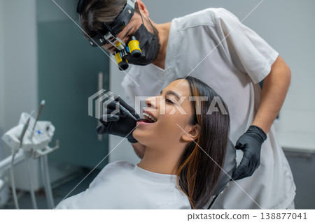 Male dentist in binocular examining oral cavity of a patient Male dentist in binocular examining oral cavity of a patient 138877041