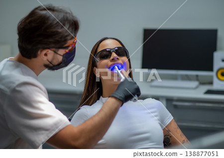 Male dentist doing tooth restoration with a photopolymer lamp Male dentist doing tooth restoration with a photopolymer lamp 138877051