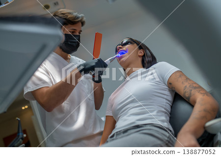 Male dentist doing tooth restoration with a photopolymer lamp Male dentist doing tooth restoration with a photopolymer lamp 138877052