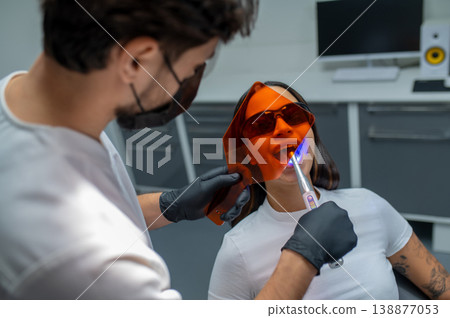 Male dentist doing tooth restoration with a photopolymer lamp Male dentist doing tooth restoration with a photopolymer lamp 138877053