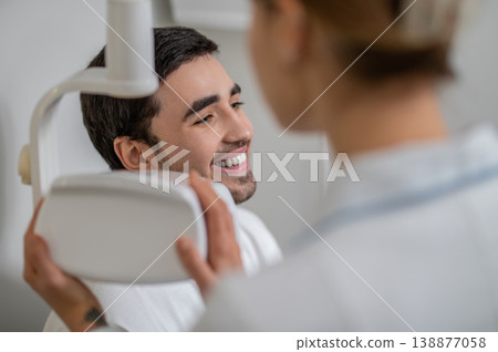 Dentist adjusting x-ray equipment near patient face Dentist adjusting x-ray equipment near patient face 138877058