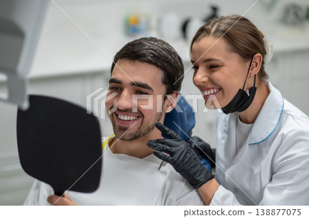 Happy patient and dentist looking at smile in mirror 138877075