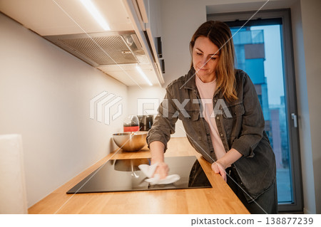 Woman cleans kitchen counter in a modern apartment during evening hours 138877239