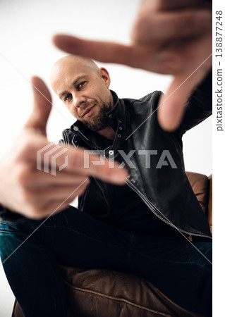 Man poses with fingers extended in a framing gesture on a leather couch in a bright room Man poses with fingers extended in a framing gesture on a leather couch in a bright room 138877248