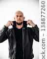 Man wearing black leather jacket stands in front of white background with hands on collar 138877260
