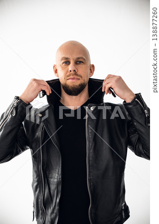Man wearing black leather jacket stands in front of white background with hands on collar 138877260