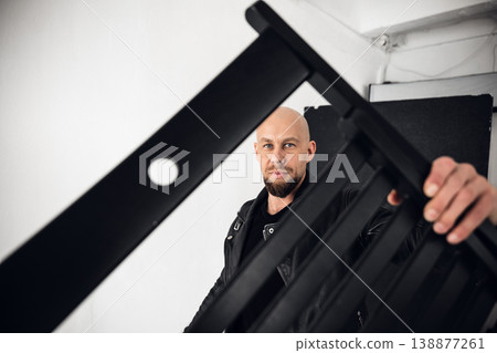 Man holds black chair in a bright indoor space while posing for a photo during daylight 138877261