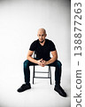 Man sits on chair in studio with plain background during a photo session in daylight 138877263