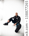 Man sits on floor wearing black leather jacket and jeans in a bright room with white walls 138877265