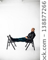 Man sits on a chair with legs stretched out on another chair in a simple studio space 138877266