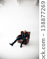 Man sits in a chair in a bright room with a simple background during a photoshoot 138877269