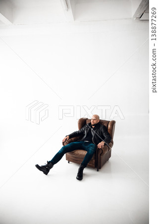 Man sits in a chair in a bright room with a simple background during a photoshoot 138877269