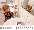 Young child washes hands in bathroom while looking in mirror 138877271