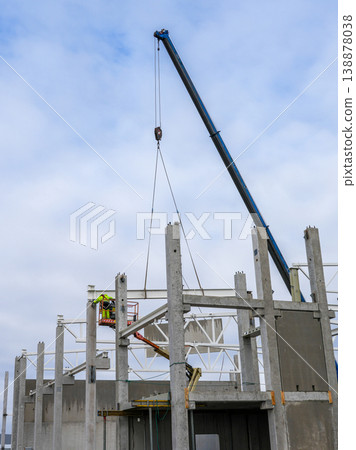 Crane lifting steel beam onto concrete columns at industrial construction site with worker on lift Crane lifting steel beam onto concrete columns at industrial construction site with worker on lift 138878038