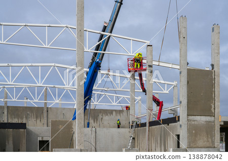 Industrial building construction with cranes lifting steel beams onto concrete frame structure Industrial building construction with cranes lifting steel beams onto concrete frame structure 138878042