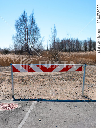 End of the road barrier with red and white stripes blocking access to gravel path in rural area 138878053