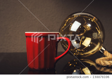 A red coffee cup sits on a table next to a glass sphere A red coffee cup sits on a table next to a glass sphere 138878106