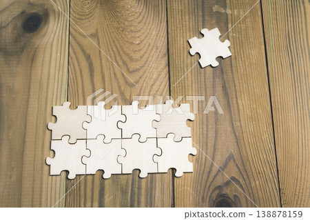 Connected puzzle pieces on a wooden table, with one piece left over. Connected puzzle pieces on a wooden table, with one piece left over. 138878159