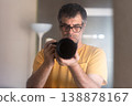 Male photographer with a professional camera taking a self-portrait in front of the mirror at home. 138878167