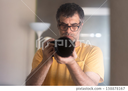 Male photographer with a professional camera taking a self-portrait in front of the mirror at home. 138878167