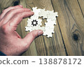 A hand is holding a puzzle piece with a gear on it 138878172