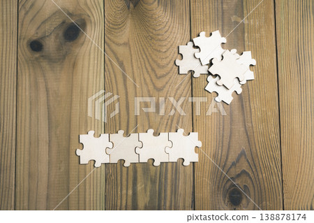 Puzzle pieces scattered across a wooden board. 138878174