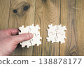 Hand holding a group of four interconnected puzzle pieces to connect them to another group on a wooden table. 138878177
