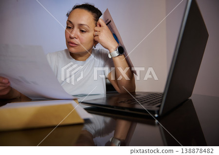 Woman Reviewing Bills and Documents at Laptop While Working From Home, Concerned About Finances Woman Reviewing Bills and Documents at Laptop While Working From Home, Concerned About Finances 138878482